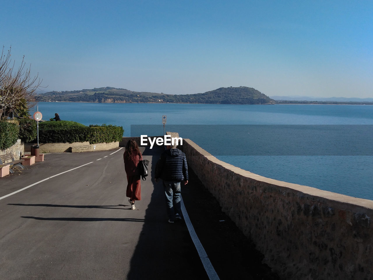 Rear view of people walking on road by sea against sky