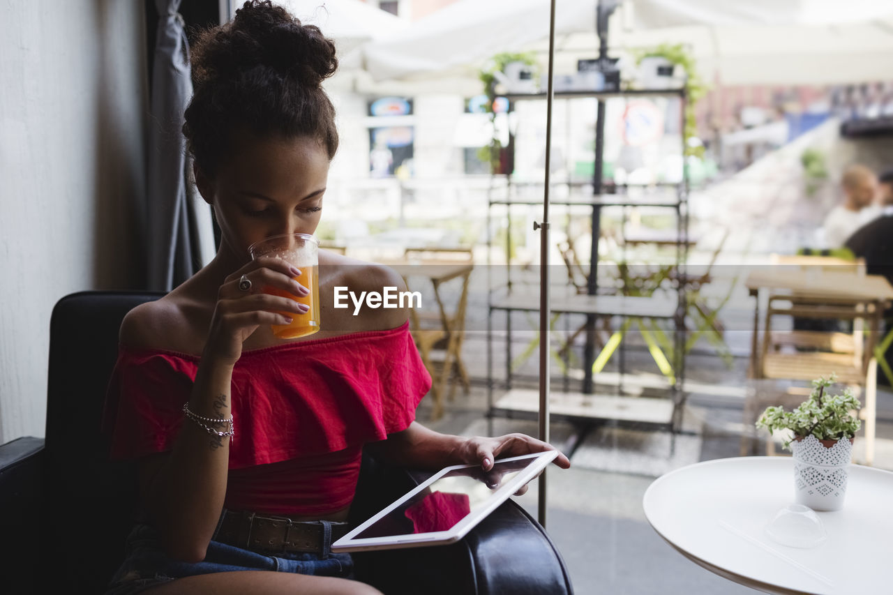 Young woman drinking glass of orange juice in a coffee shop looking at tablet