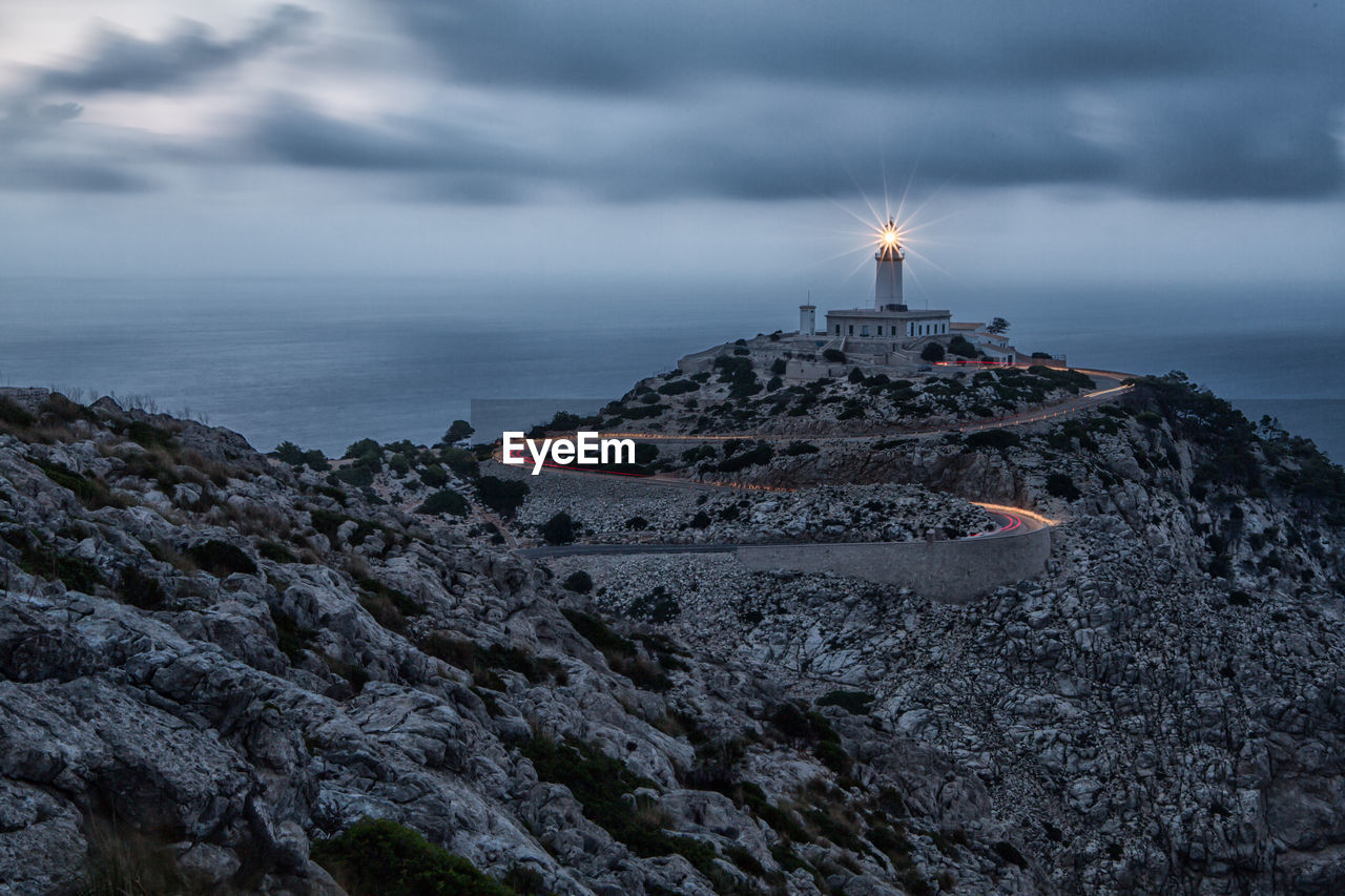 Lighthouse on cliff by sea against sky