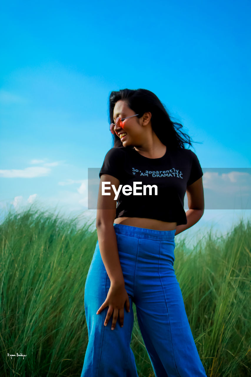 WOMAN STANDING ON FIELD AGAINST SKY