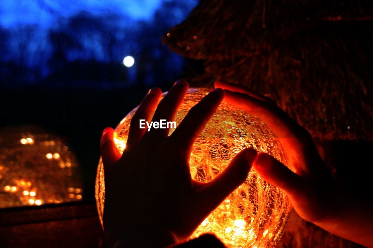 CLOSE-UP OF HAND HOLDING LIT CANDLE AGAINST SKY