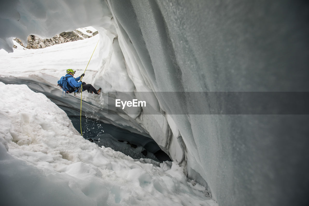 Mountaineer rappels into glacier cave.
