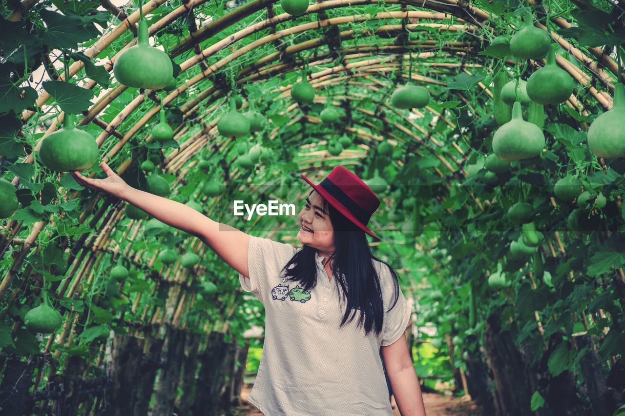 FULL LENGTH OF WOMAN WEARING HAT STANDING AGAINST PLANTS