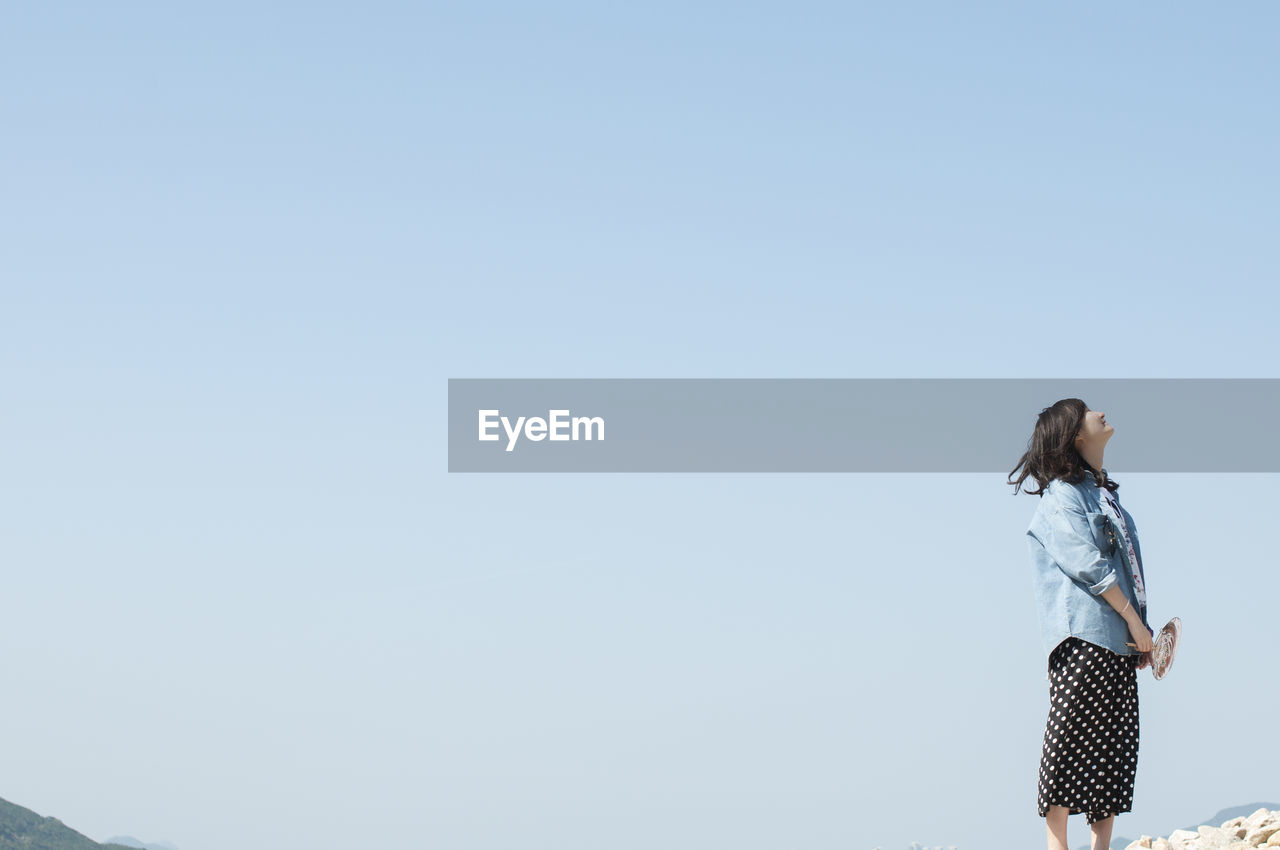 Woman looking up while standing against clear sky