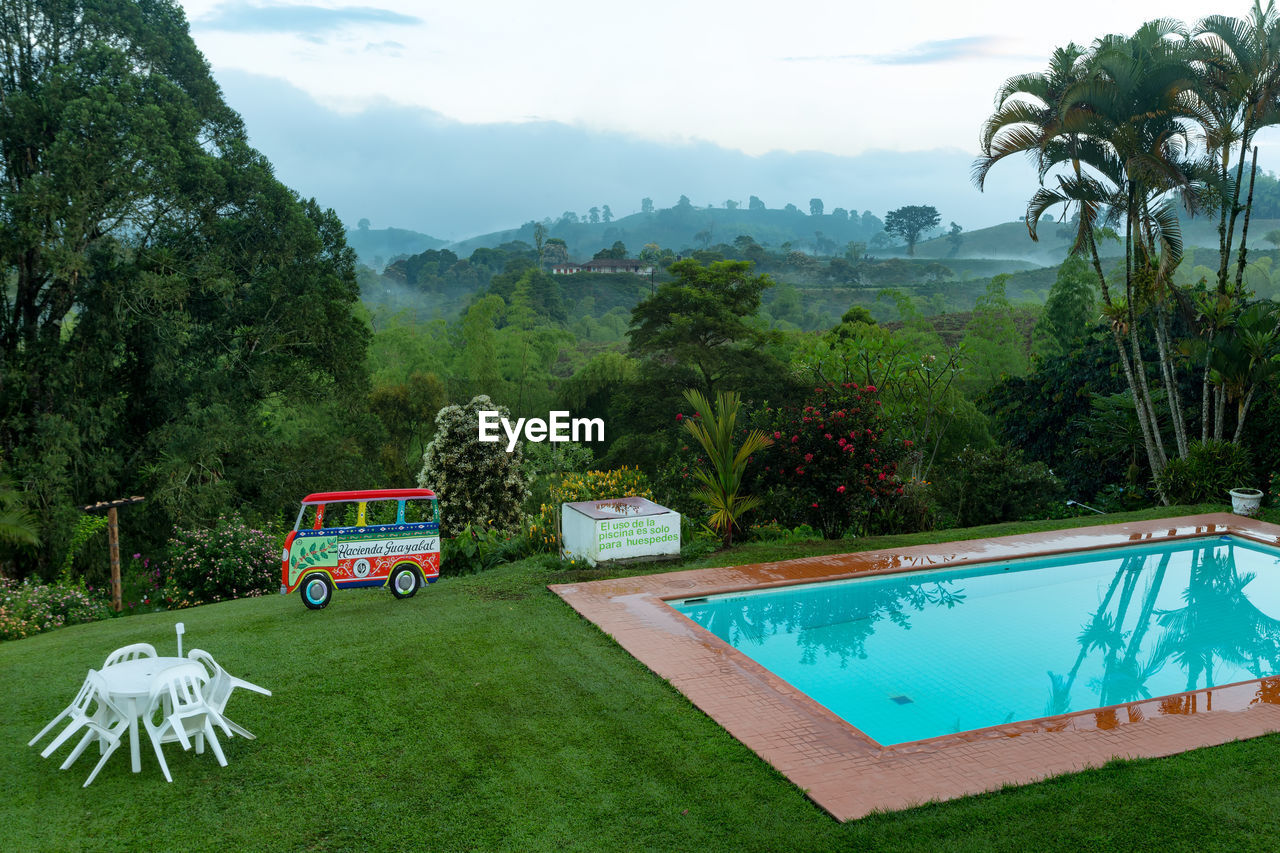 SWIMMING POOL BY TREES AGAINST MOUNTAINS