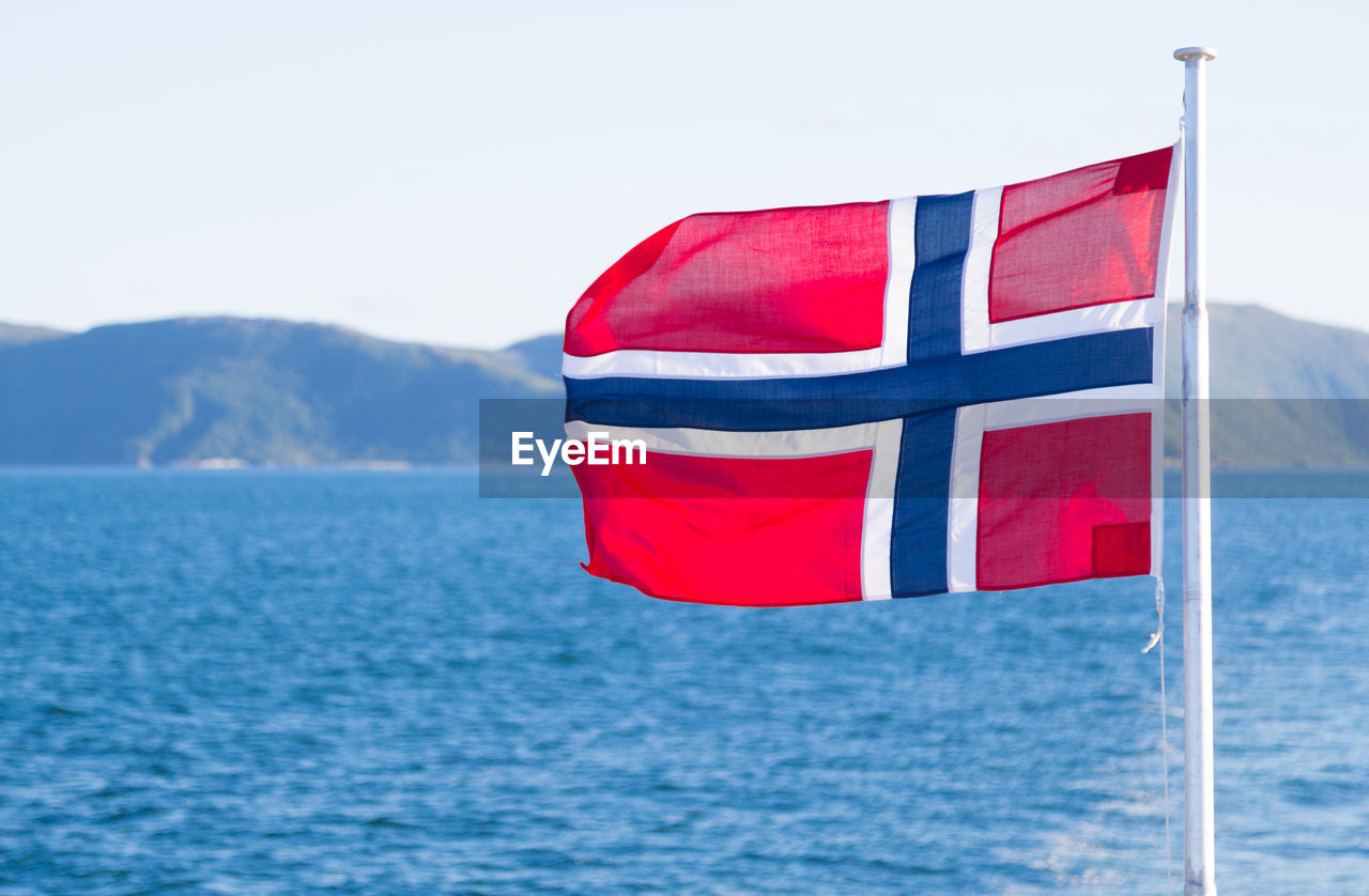 Norwegian flag waving by sea against sky