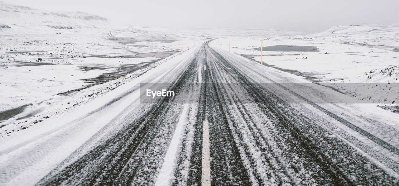 Snow covered road amidst landscape against sky