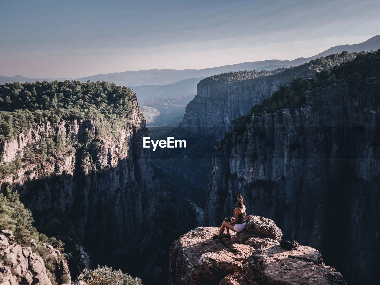 Girl sitting on rock by mountains against sky