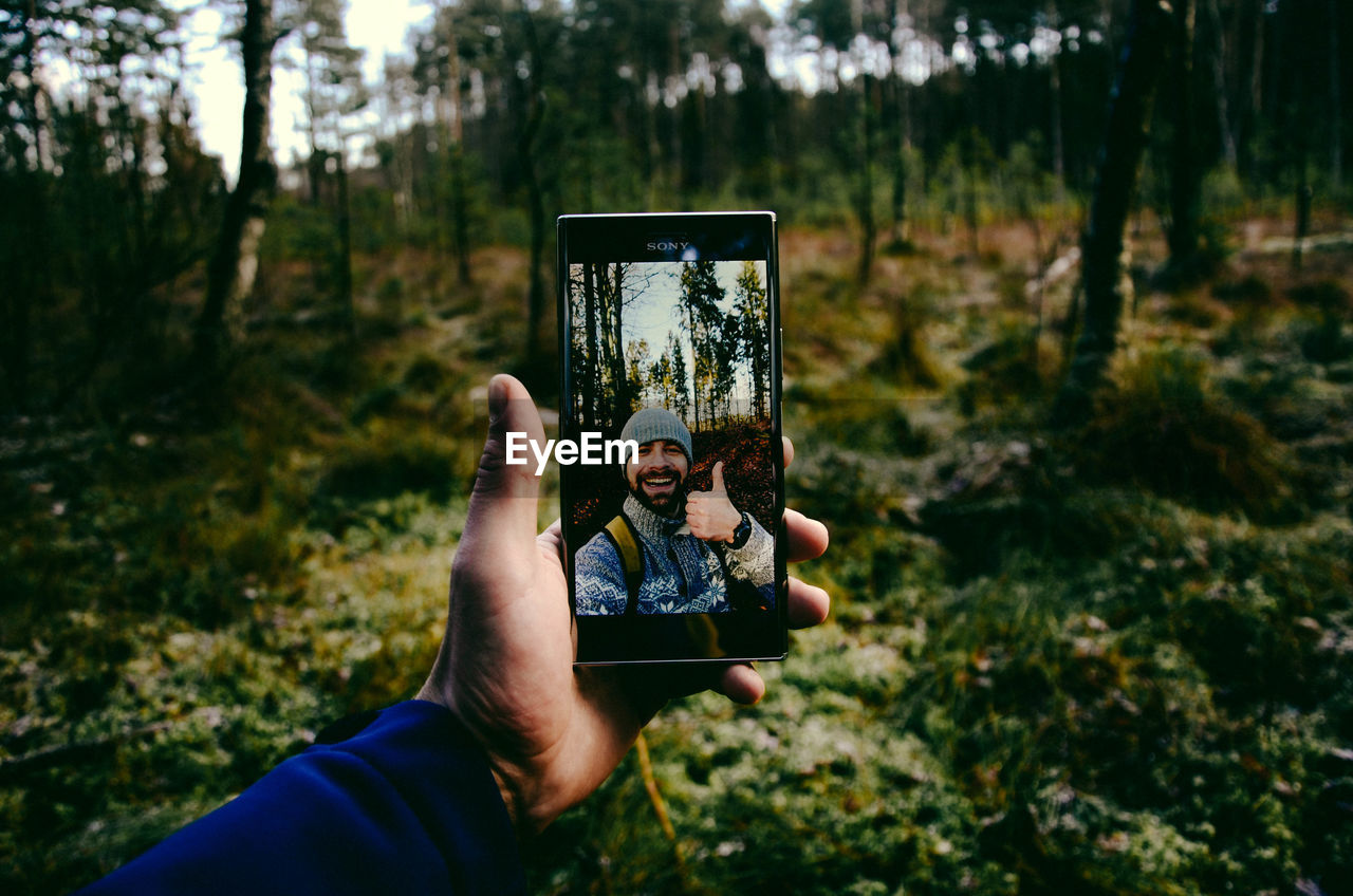 Cropped hand of man taking selfie in forest