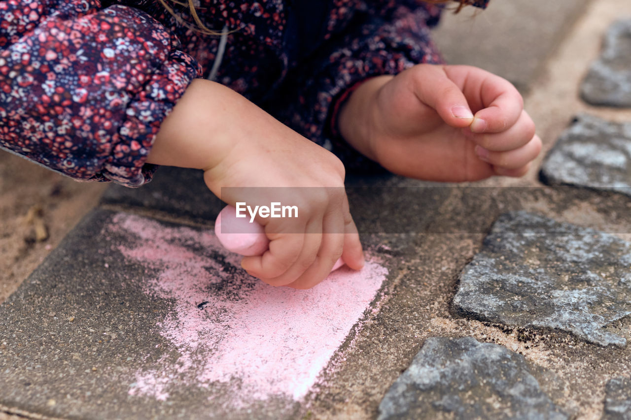 Cropped hands of girl drawing on footpath