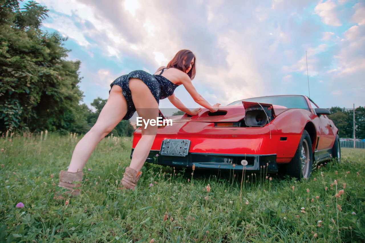 Woman leaning on car at field