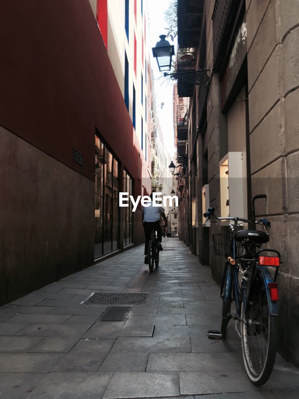 REAR VIEW OF MAN RIDING BICYCLE ON STREET IN CITY