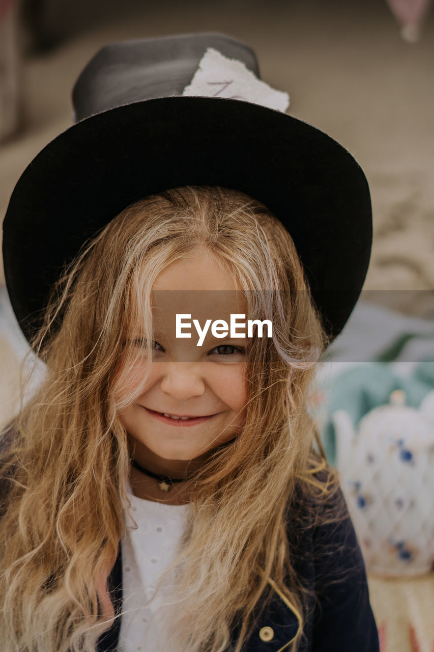 Child girl in jacket and top hat smiling and looking at the camera at the beach