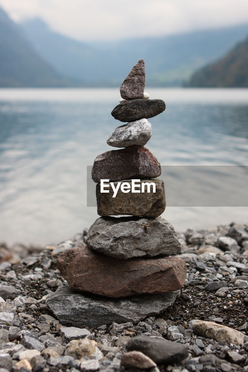 Stack of stones in sea against sky on sunny day