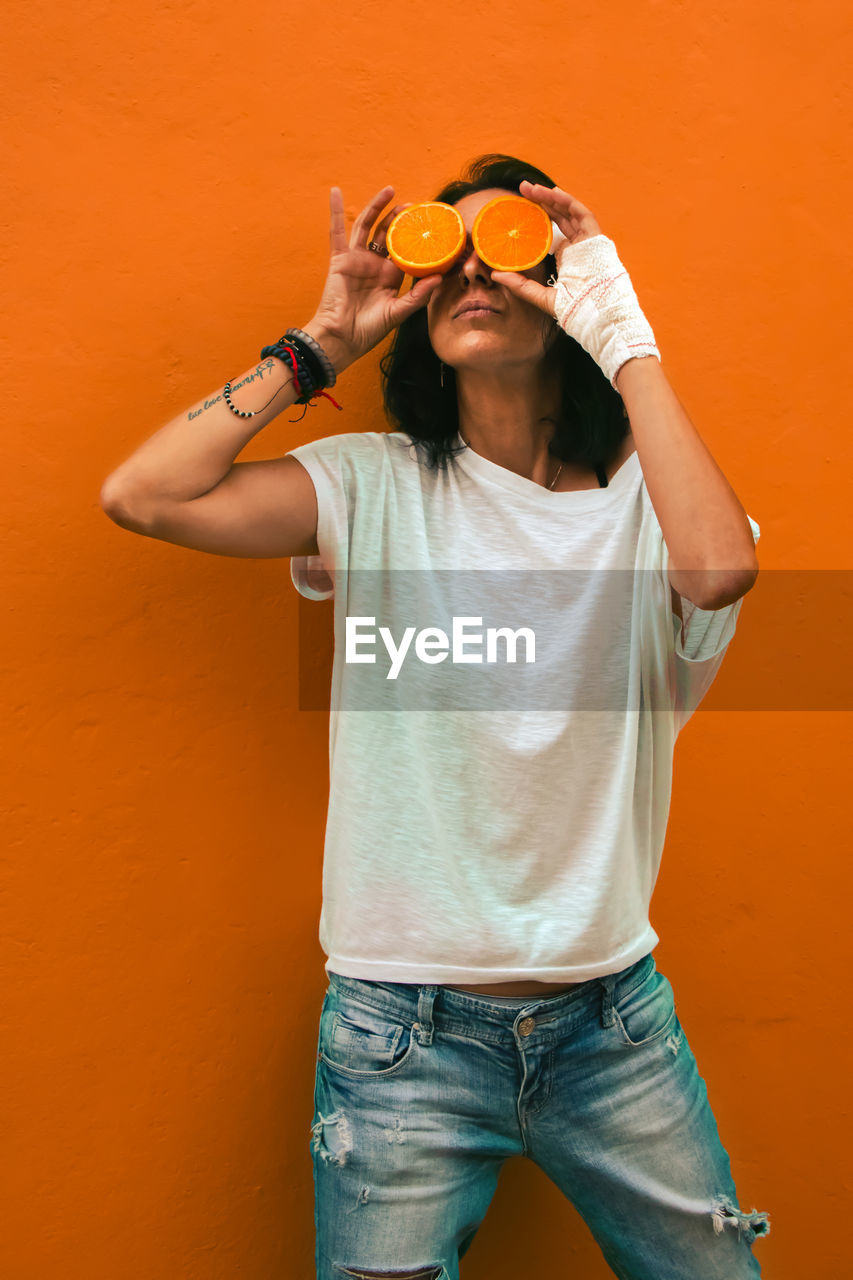 Woman covering face with orange while standing against orange background