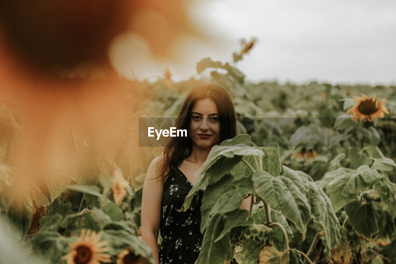 Young woman standing amidst sunflowers on field against sky