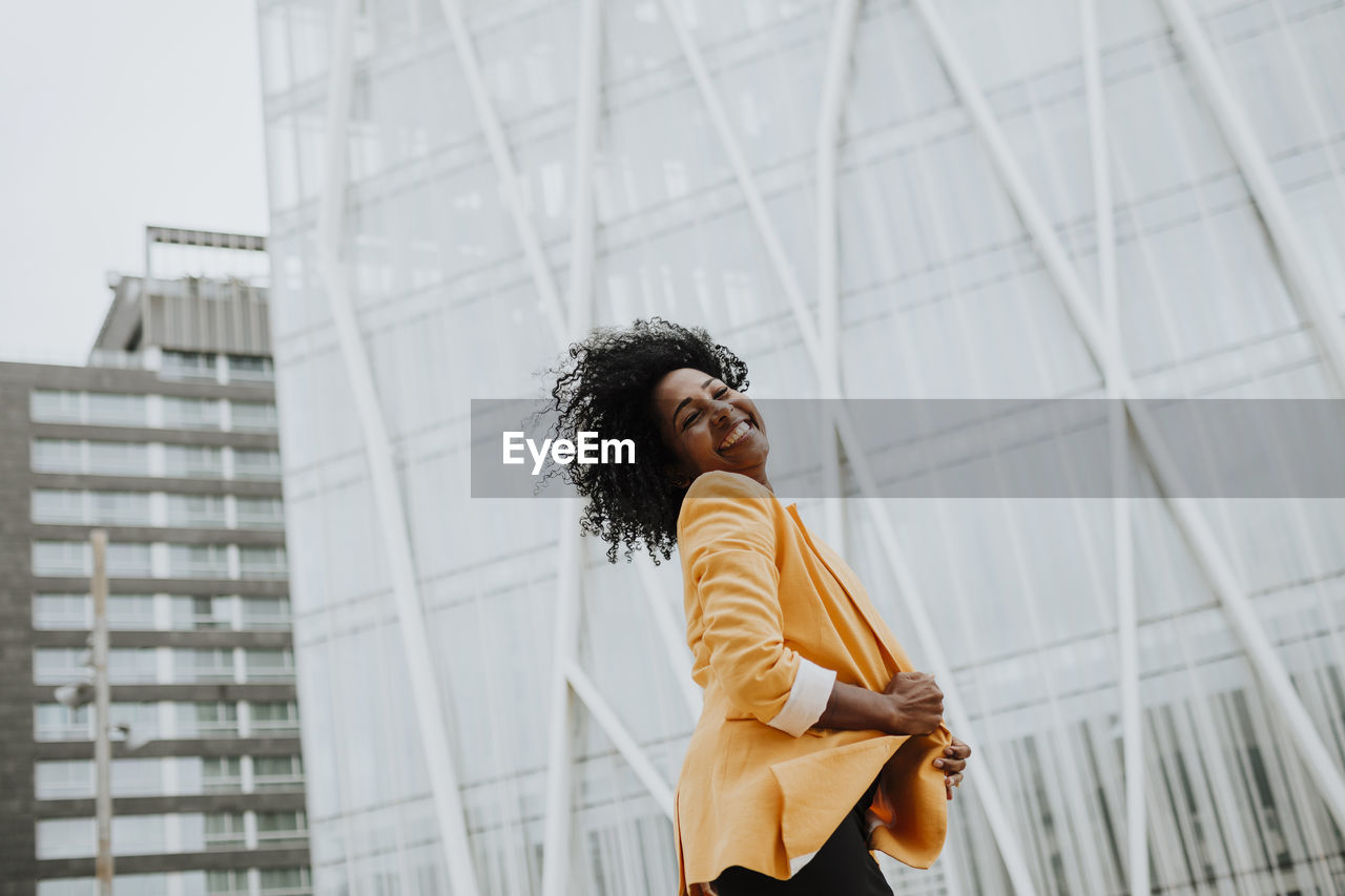 Smiling female entrepreneur with eyes closed standing against office building