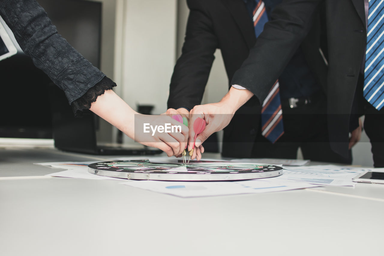 Colleagues holding dart on bull-eye at table in office