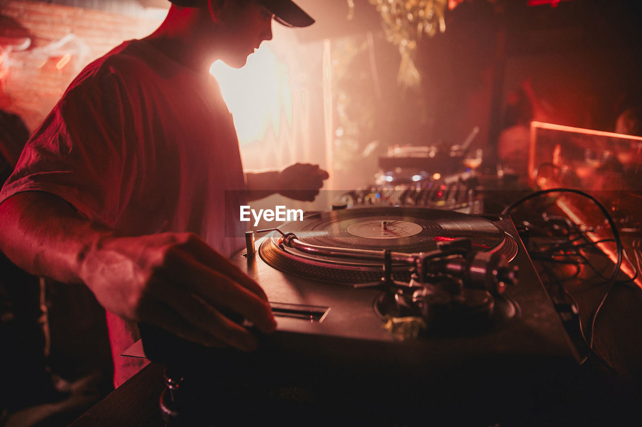 Side view of crop male dj mixing music on controller during concert in dark nightclub