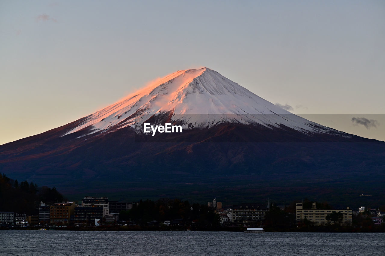 mountain, volcano, stratovolcano, sky, travel destinations, horizon, nature, beauty in nature, landscape, water, scenics - nature, dawn, architecture, snowcapped mountain, no people, snow, city, cold temperature, culture, winter, travel, sunrise, mountain peak, environment, land, outdoors, building exterior, built structure, tourism, morning, sea, cinder cone, tranquility, volcanic landscape