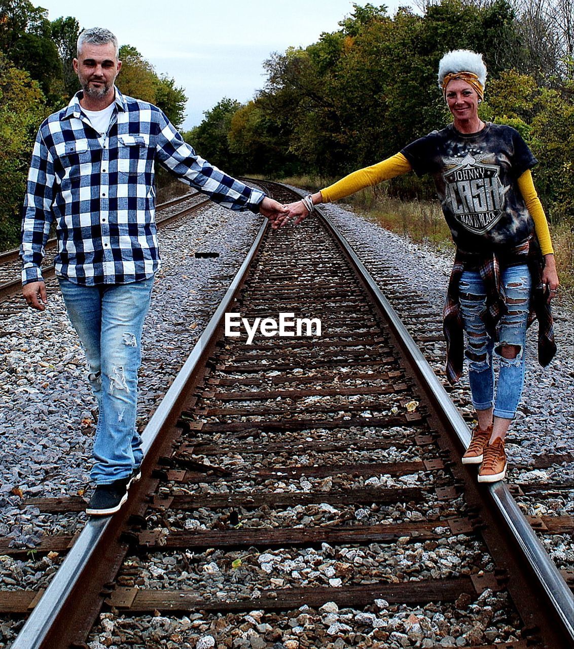 Front view of a happy couple walking on railroad track