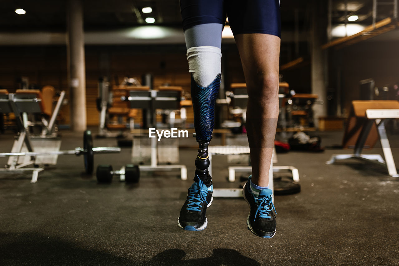 Low section of man with prosthetic leg jumping in gym