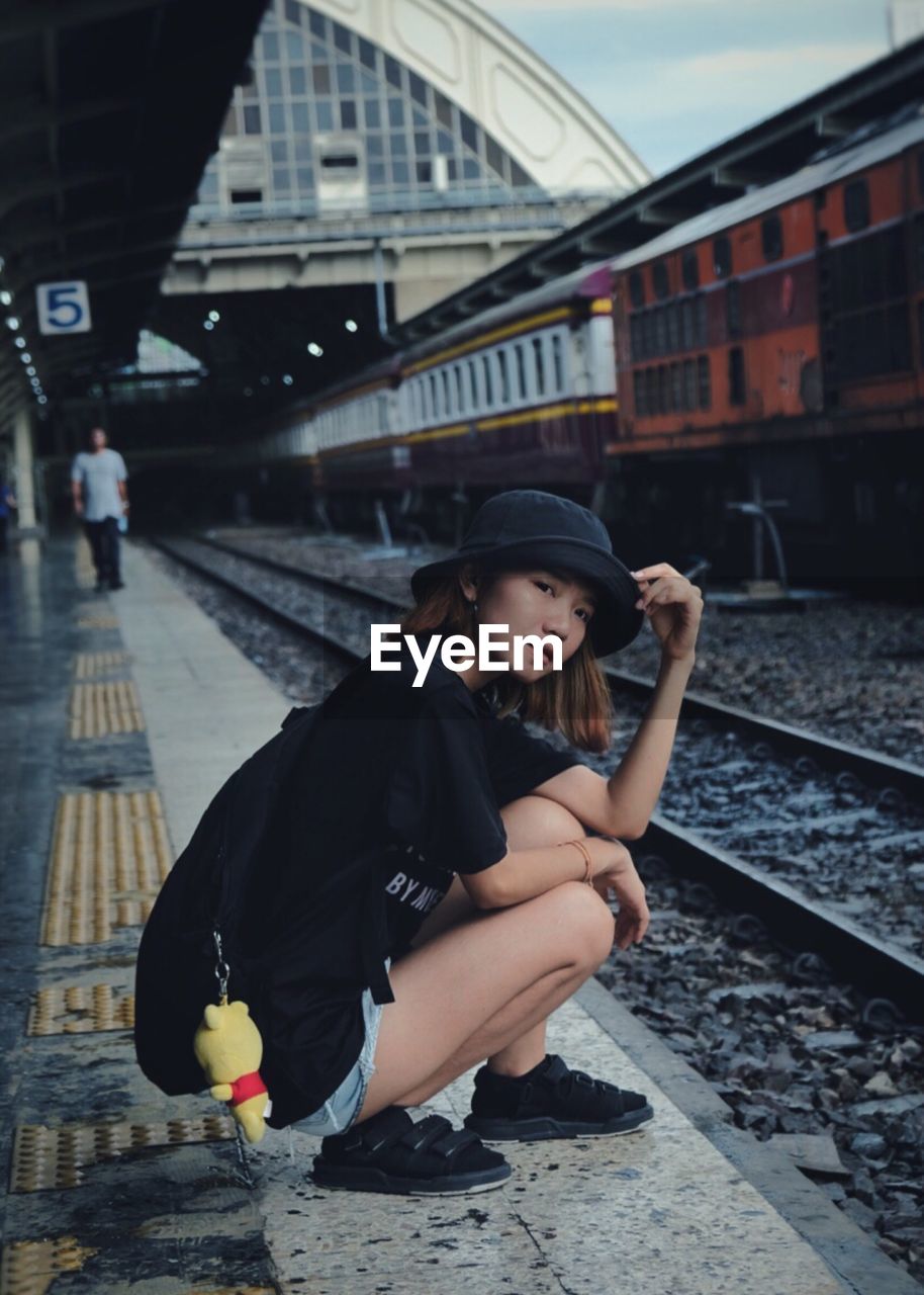 Portrait of woman crouching at railroad station platform in city