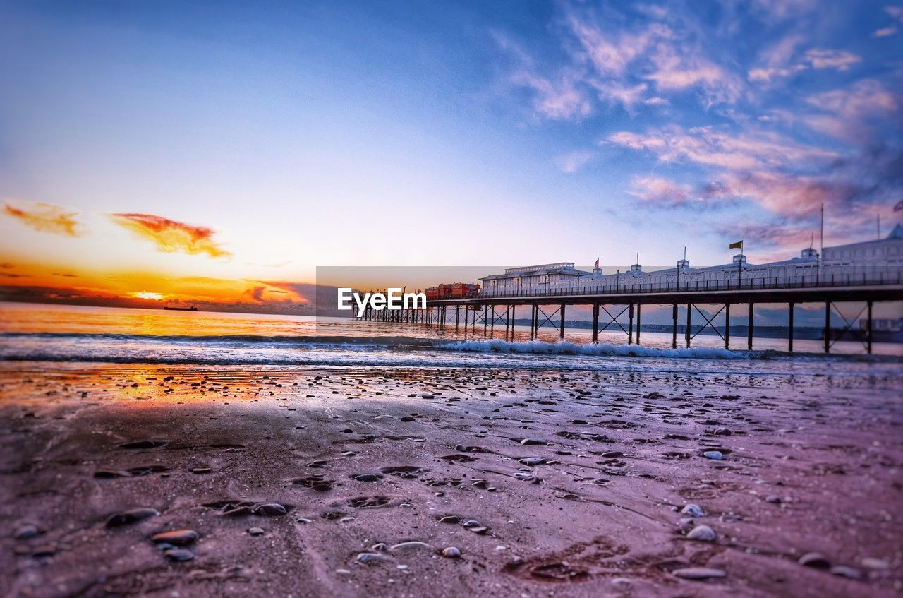 pier on beach against sky during sunset