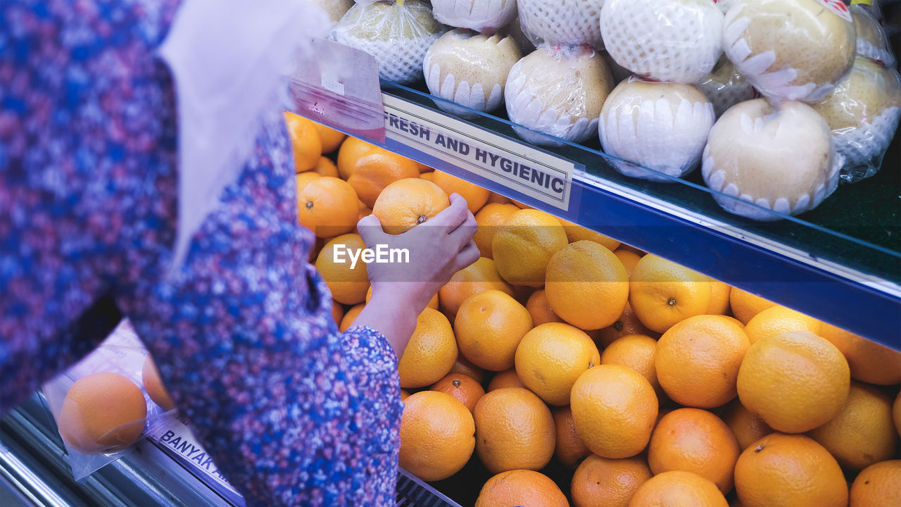 Young woman choosing fresh oranges in supermarket