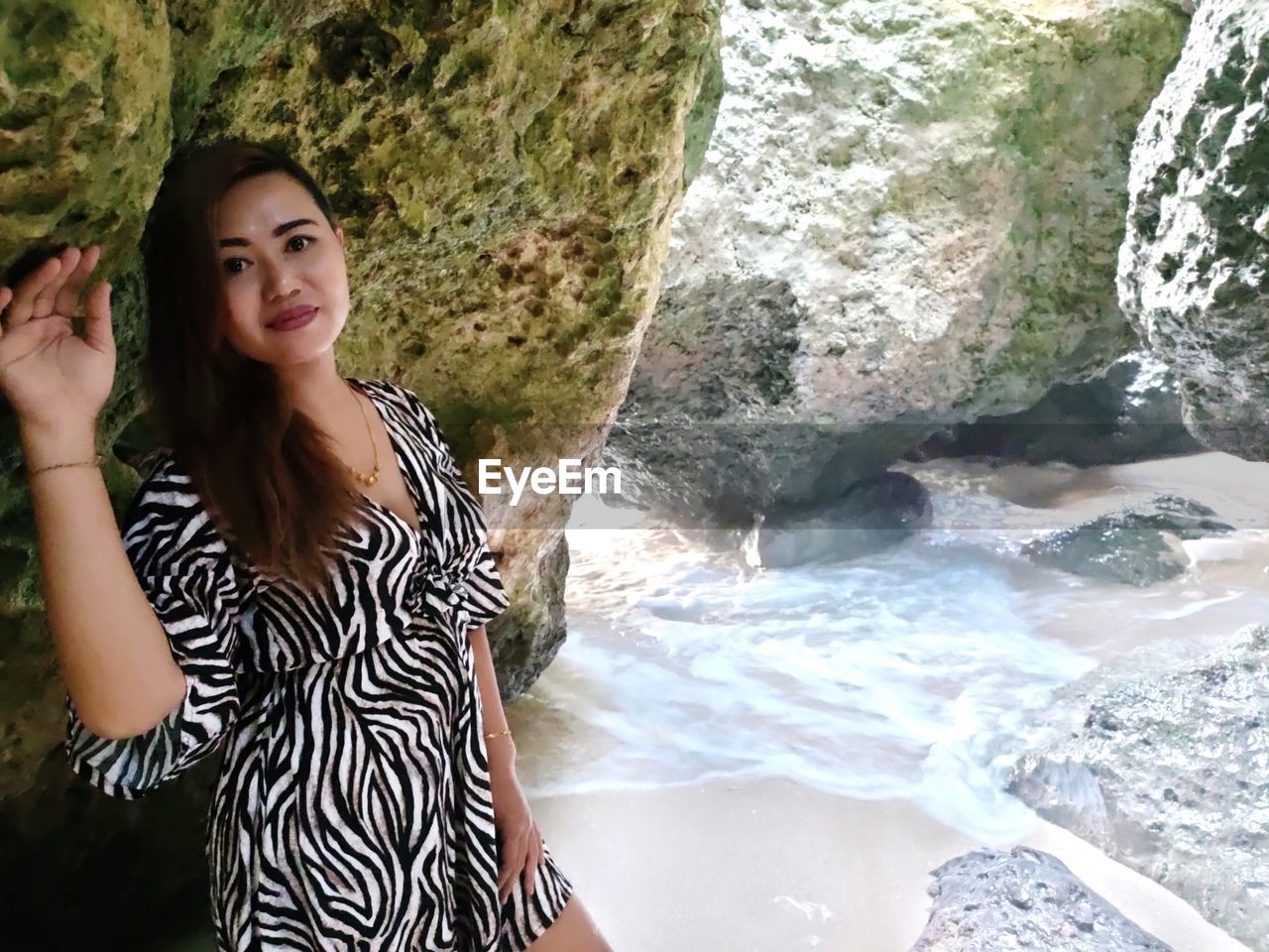 PORTRAIT OF YOUNG WOMAN STANDING ON ROCK AT WATERFALL