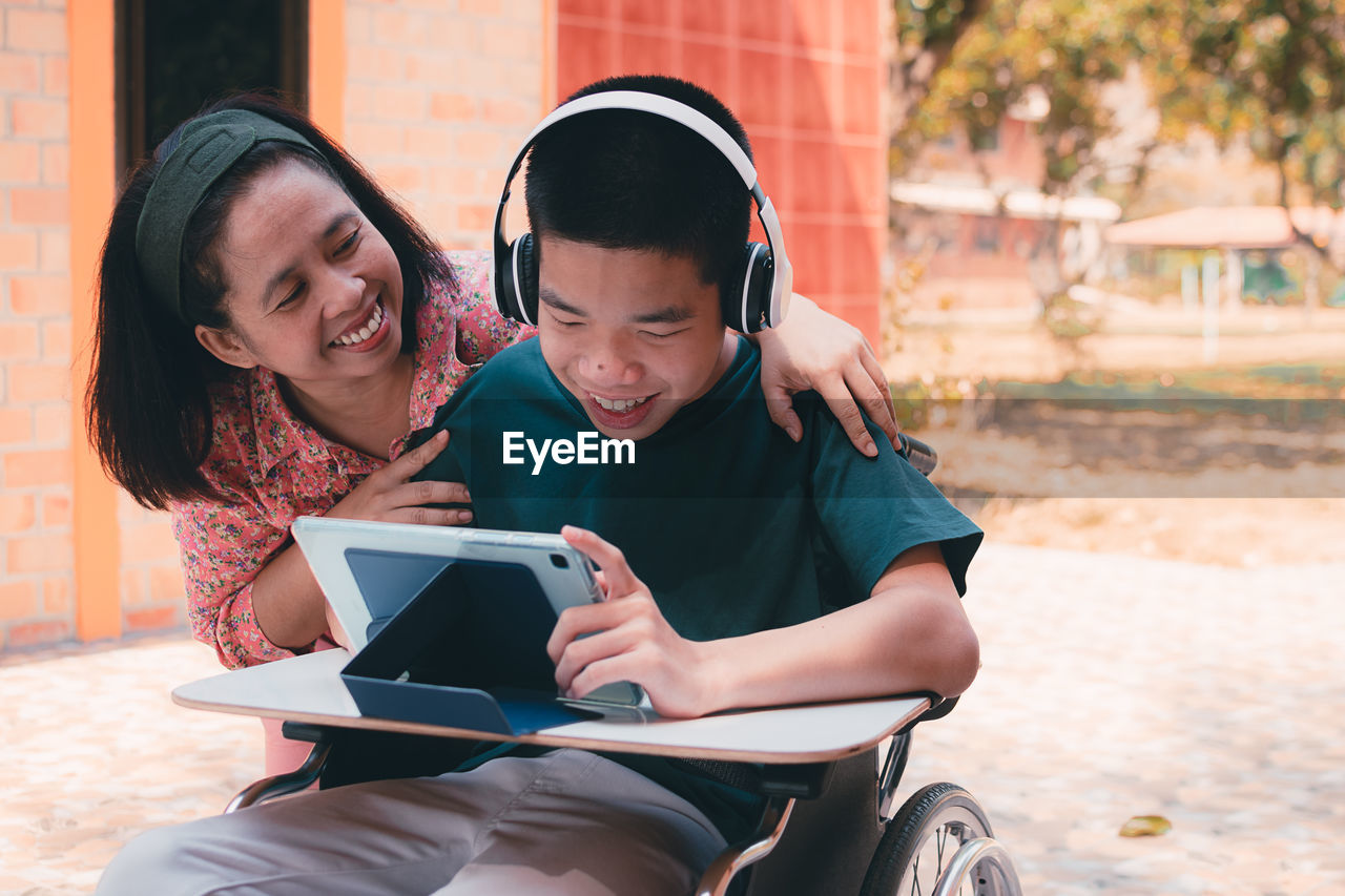 Portrait of a smiling  disabled child on wheelchair using technology with parent.