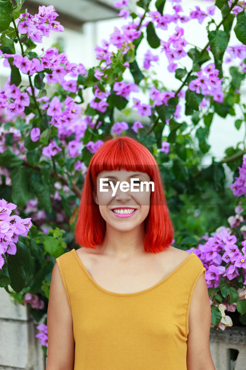 Portrait of smiling woman standing against pink flowering plants