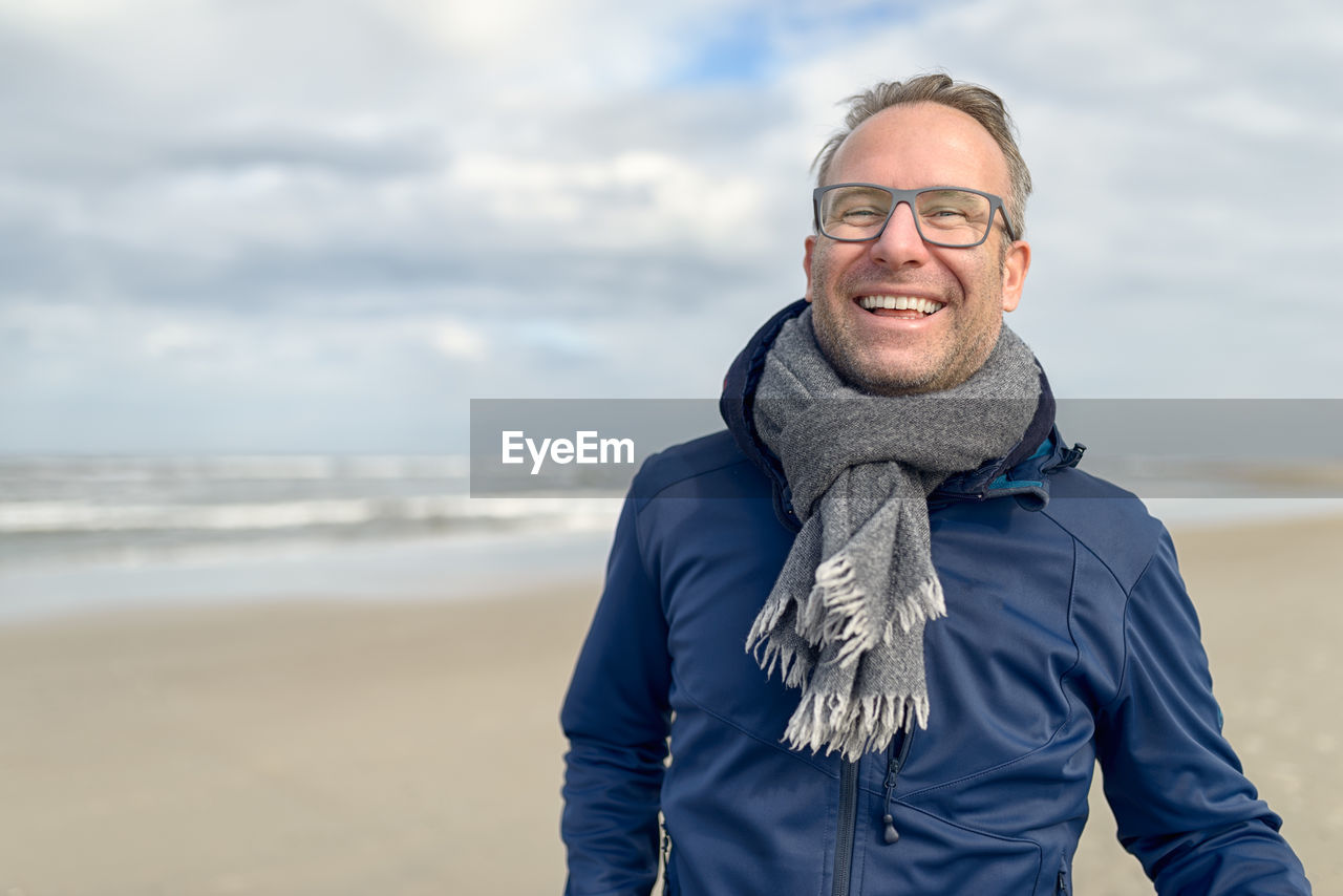 Smiling man standing on sea shore at beach against cloudy sky