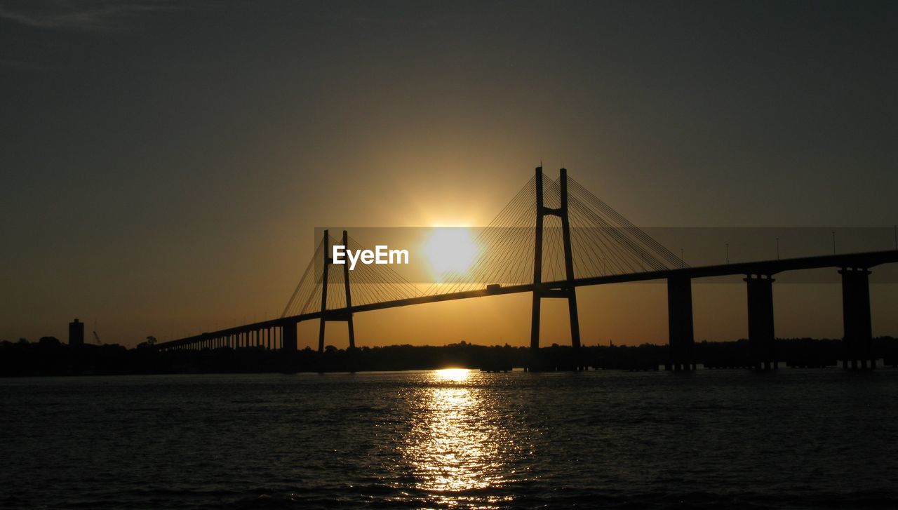 Silhouette bridge over sea against sky during sunset