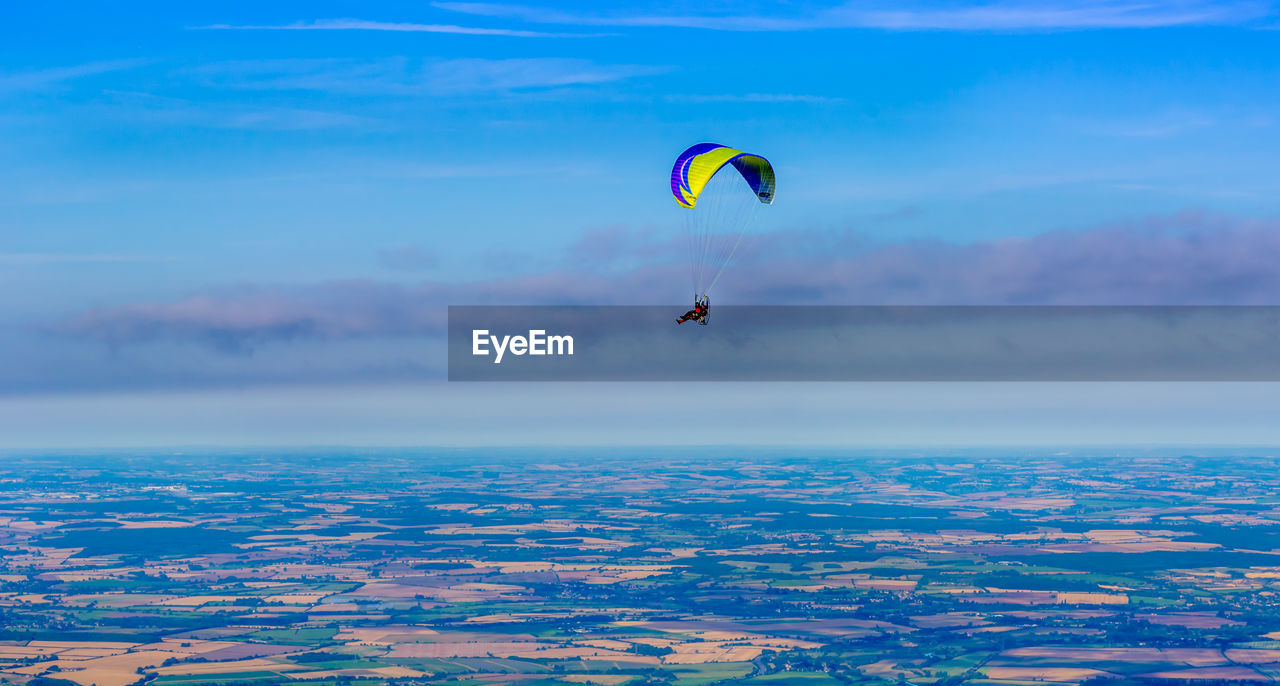 Person paragliding over farm land against sky