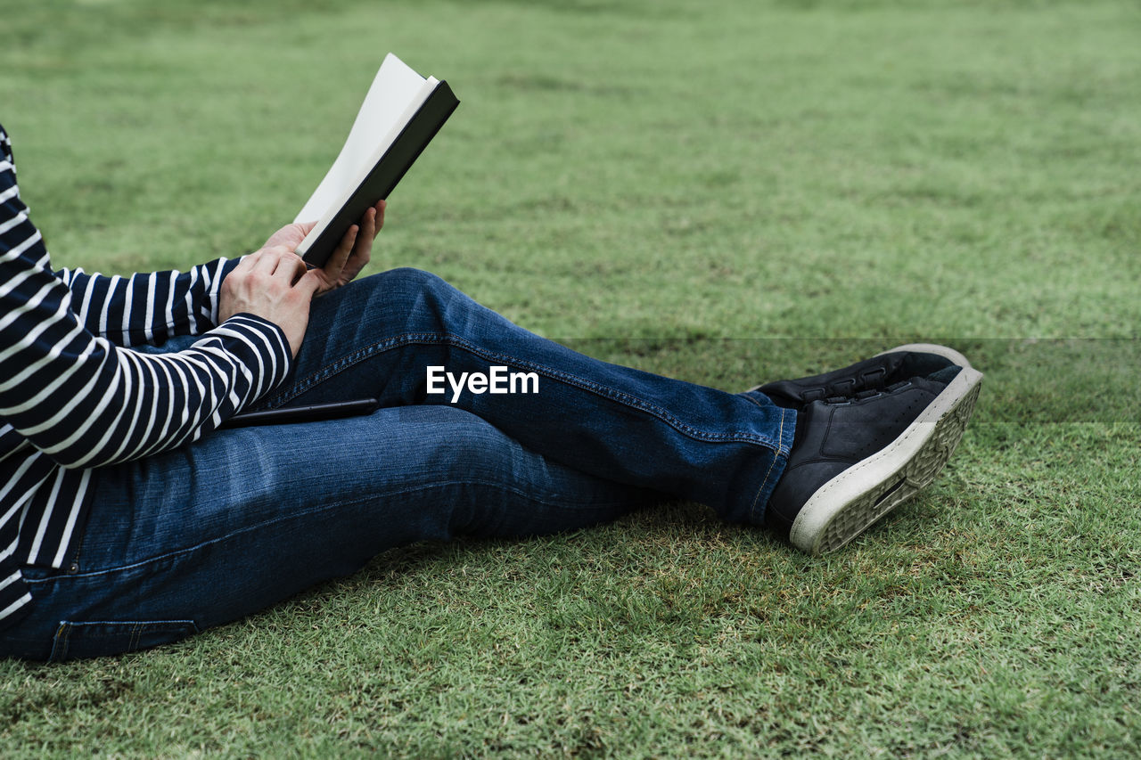 Low section of man holding book on lawn