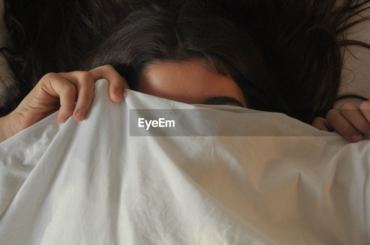 Close-up of woman lying on bed and covering face with fabric