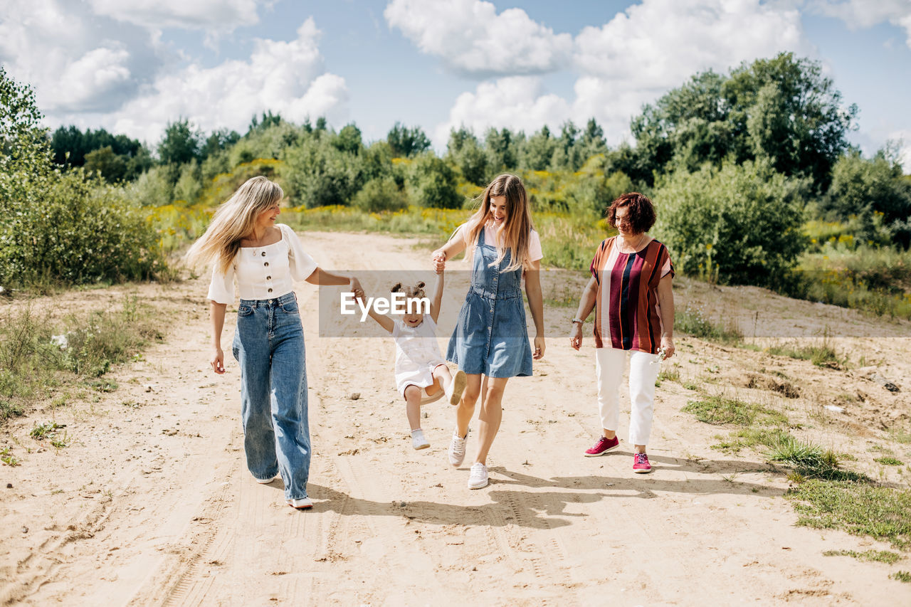 Several generations of women of the same family are walking along a dirt road outside the city