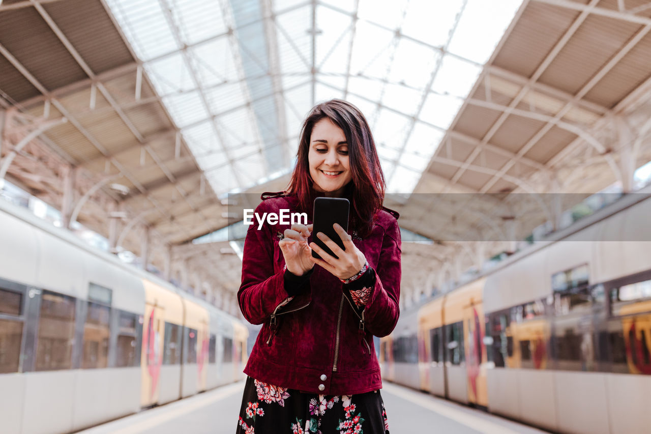 Smiling woman using mobile phone while standing at railroad station platform