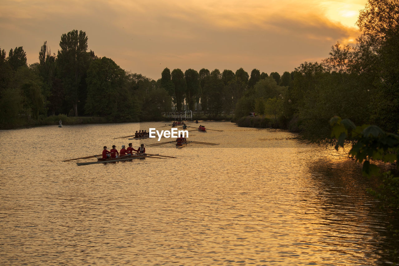 People on boat rowing in river against sky during sunset eton college bumps race