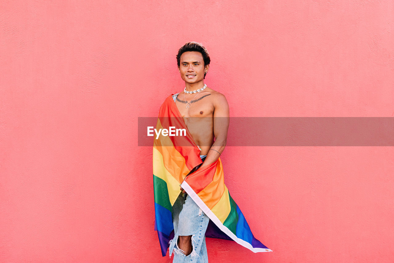 Gay man with rainbow flag against pink background