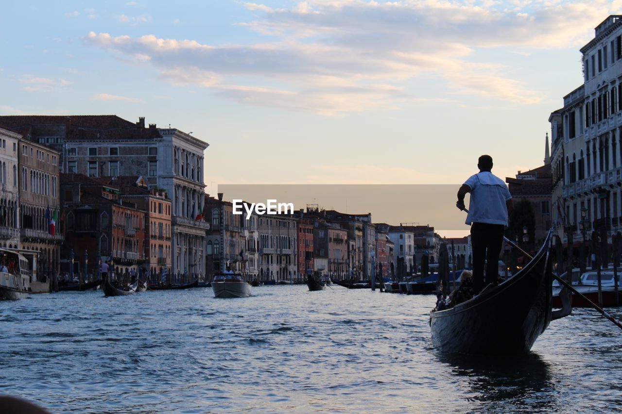 MAN STANDING ON WOODEN POSTS IN CANAL AGAINST SKY