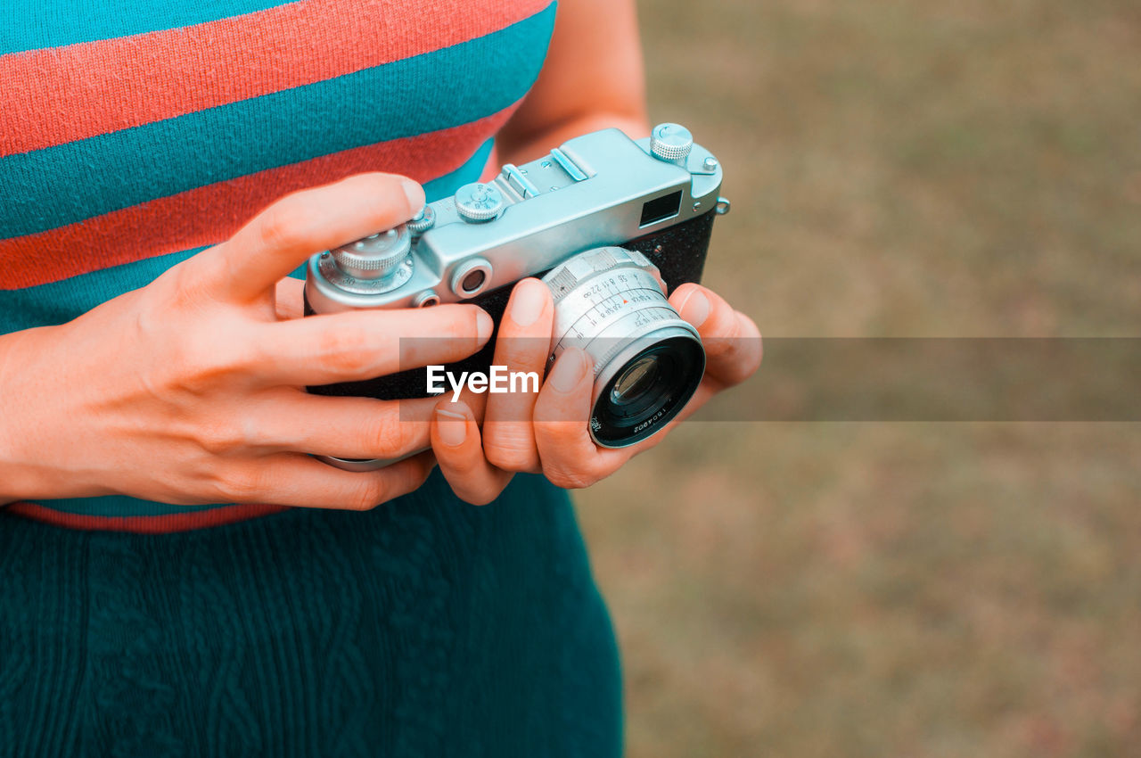 Midsection of woman holding camera while standing outdoors