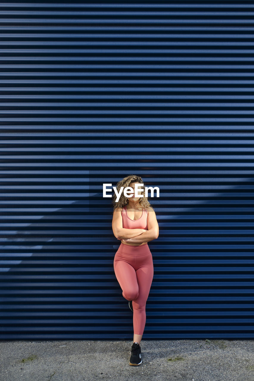 Confident sportswoman with arms crossed leaning on blue wall