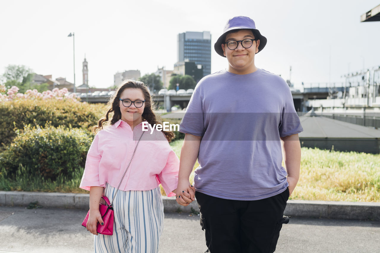 Smiling brother holding hand of sister with down syndrome standing on footpath