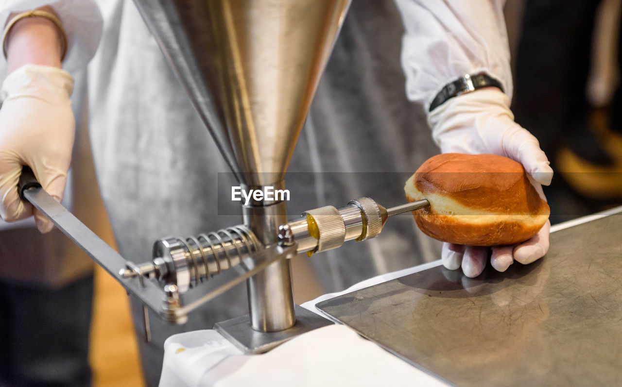 Midsection of man using appliance while filling donut at factory