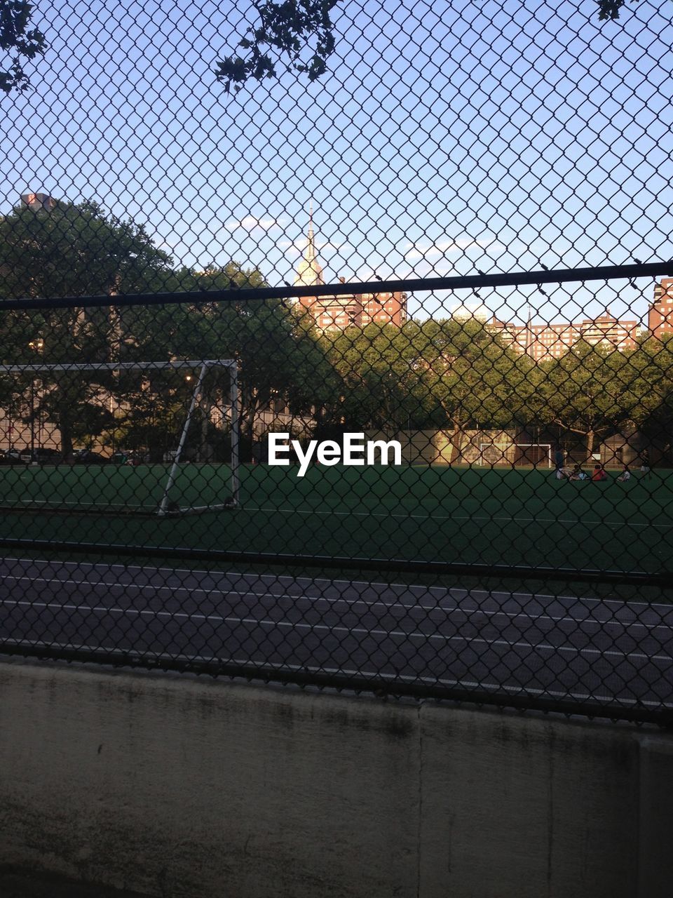 View of goal net on grass field through fence