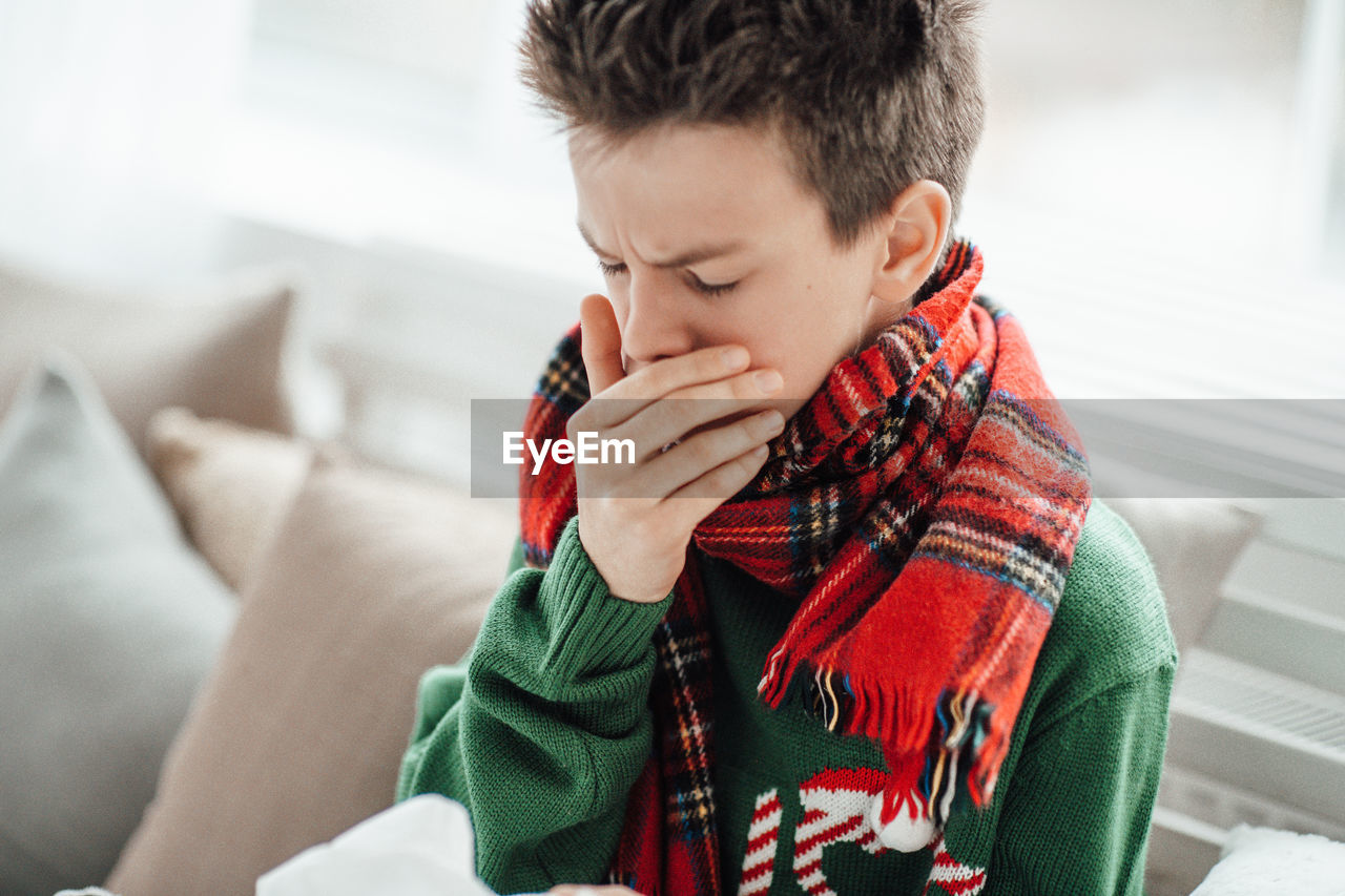 Close-up of boy sneezing at home