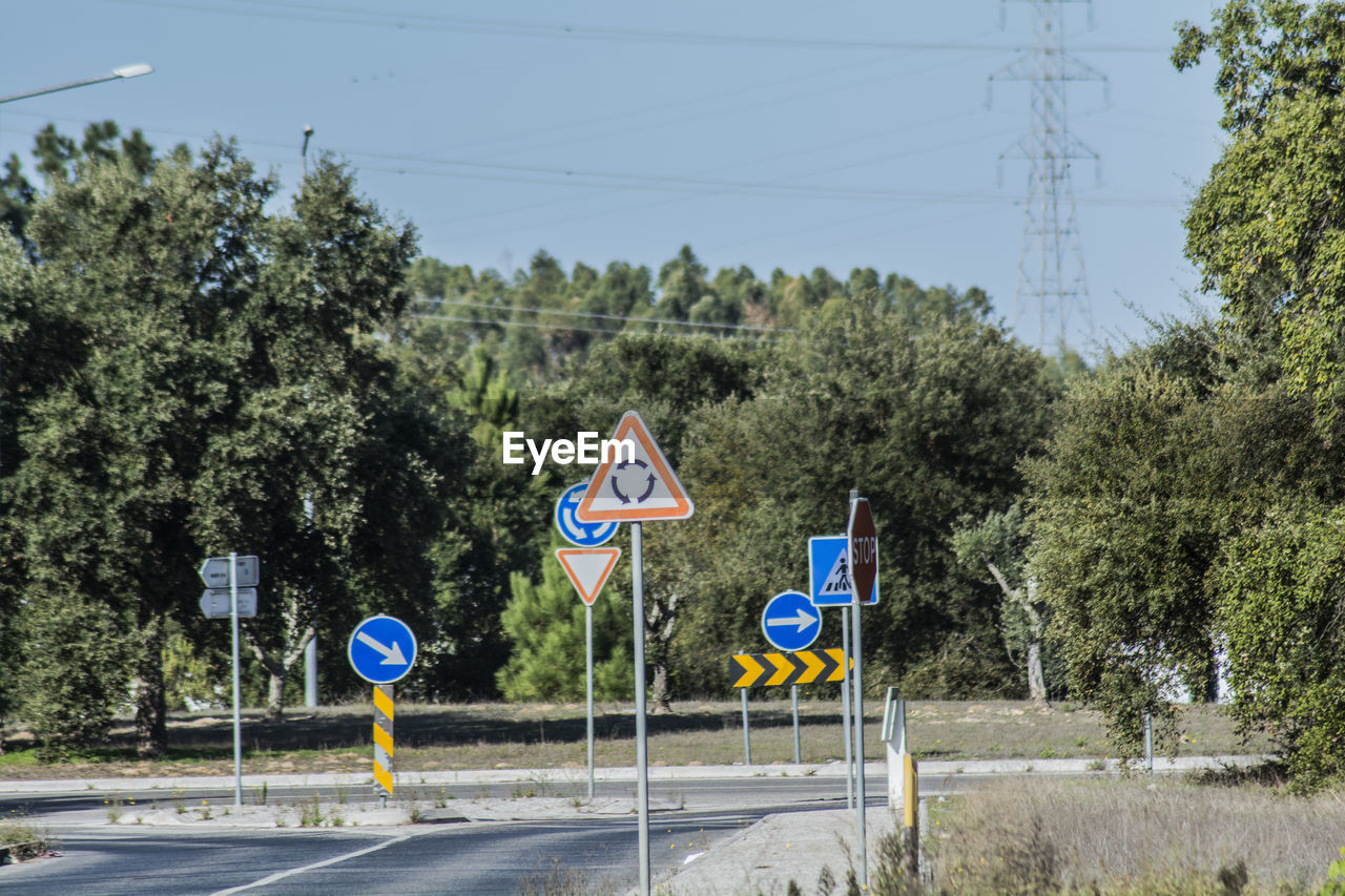 Road sign by trees against sky