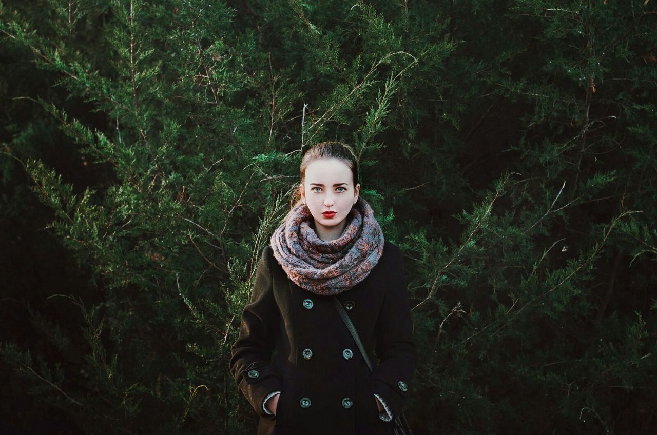 PORTRAIT OF YOUNG WOMAN STANDING BY TREE IN SUNLIGHT